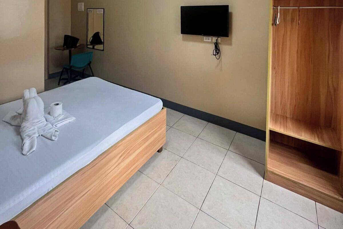 Ein Hotelzimmer mit Bett, Fernseher, Kleiderschrank und einem kleinen Schreibtisch mit Stuhl.