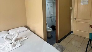 Een hotelkamer met een bed, een badkamer zichtbaar door een open deur, en een klein tafeltje met een stoel.