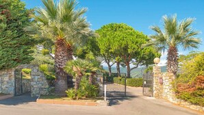 A gated entrance with stone walls, palm trees, and a clear sky. - Holiday apartment mit Klimaanlage und Pool (Marina di Andora)
