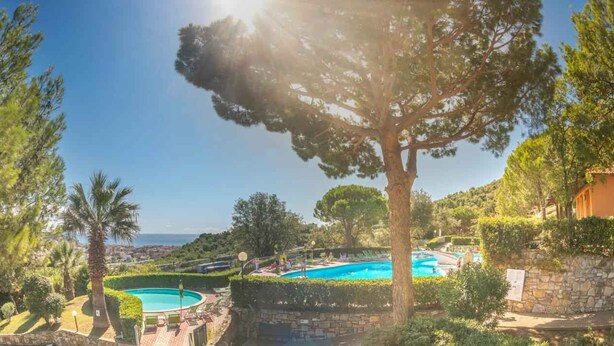 Área da piscina com muro de pedra, uma grande árvore e vista para o mar.