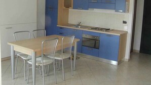 Een moderne keuken met blauwe kastjes, een roestvrijstalen oven en een eethoek met een houten tafel en metalen stoelen.
