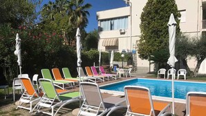 A poolside area with lounge chairs and umbrellas, a swimming pool, and a building with balconies. - Holiday apartment mit Klimaanlage und Pool (Loano)