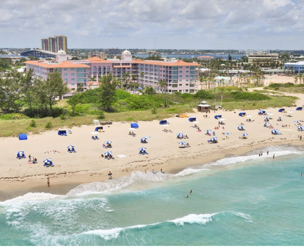 Une plage avec des parasols et des gens, un hôtel avec un dôme et de nombreux étages, et une vue dégagée sur l’océan.