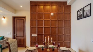 A dining area with a wooden partition, a table set for four, and a sofa in the background. - Elivaas Konifer Greyvine Hillside 9 BHK  (Kasauli)