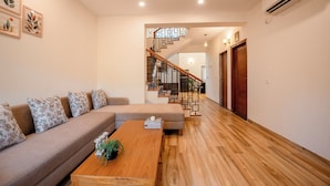 A modern living room with a wooden floor, a sofa, a coffee table, and a staircase with a geometric railing. - Staymaster Terra Nusa 4BR Villa (Colvale)