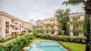 A residential building with a swimming pool, surrounded by lush greenery and palm trees. - Staymaster Terra Nusa 4BR Villa (Colvale)
