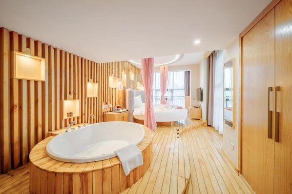 Una habitación de hotel moderna con suelo de madera, una bañera grande, una cama y un televisor.