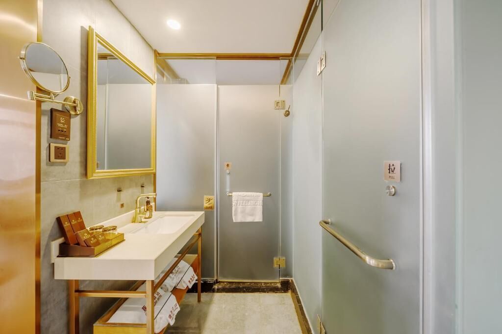 Un bagno con un lavabo bianco, accessori dorati, uno specchio e un box doccia in vetro.