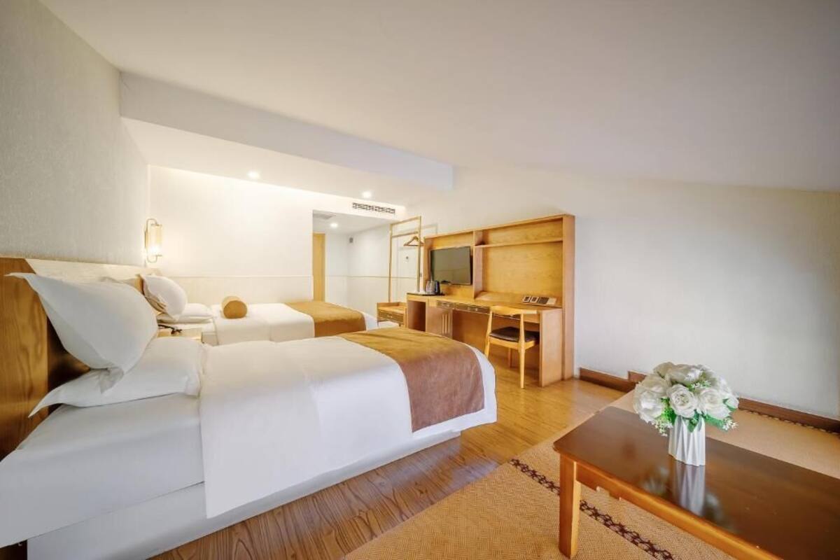 A hotel room with two beds, a desk, a chair, a small table, and a vase with flowers.