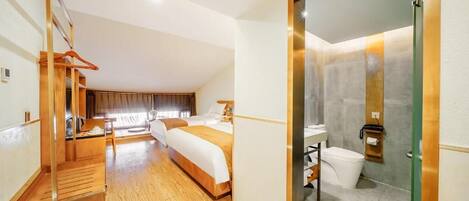 A hotel room with a wooden staircase, a large bed, a bathroom with a glass shower enclosure, and a view of the outdoors.