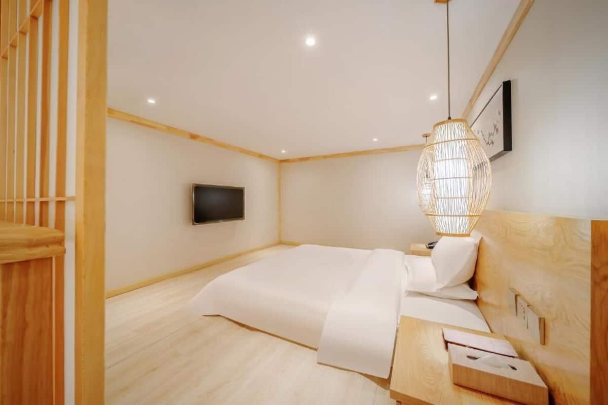 A bedroom with a bed, bedside table, wooden headboard, wall-mounted TV, and a hanging light fixture.