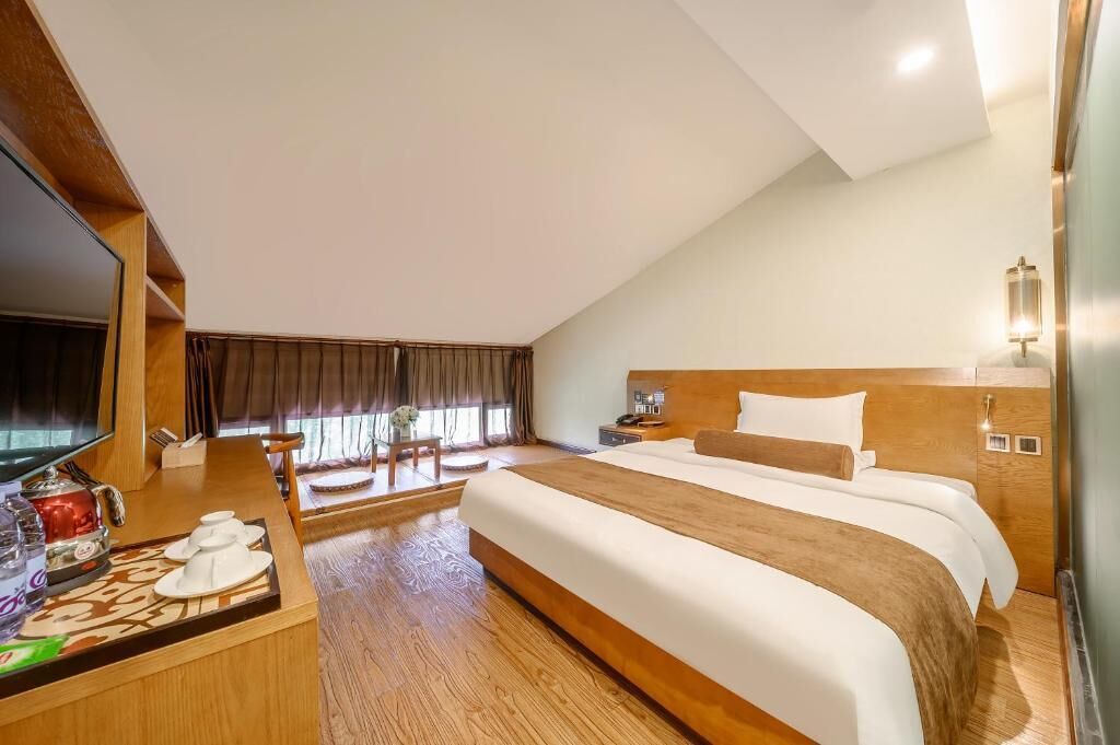 Habitación de hotel con una cama grande, un escritorio con televisor y una ventana con cortinas.