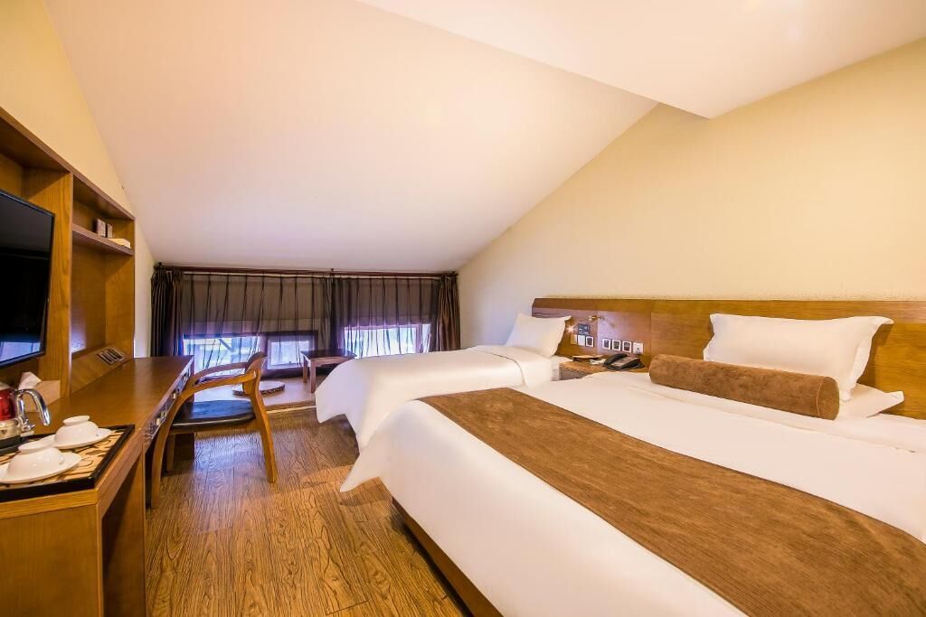 Una habitación de hotel con una cama grande, un escritorio con silla, televisor y ventana con cortinas.