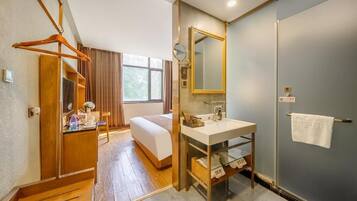Una habitación de hotel con una cama, un baño con lavabo y espejo, y un armario de madera.
