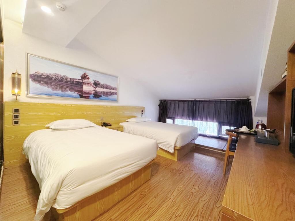 Une chambre d’hôtel avec deux lits, un plancher en bois, un tableau au mur, une fenêtre avec des rideaux et une petite table sur laquelle sont posés quelques objets.
