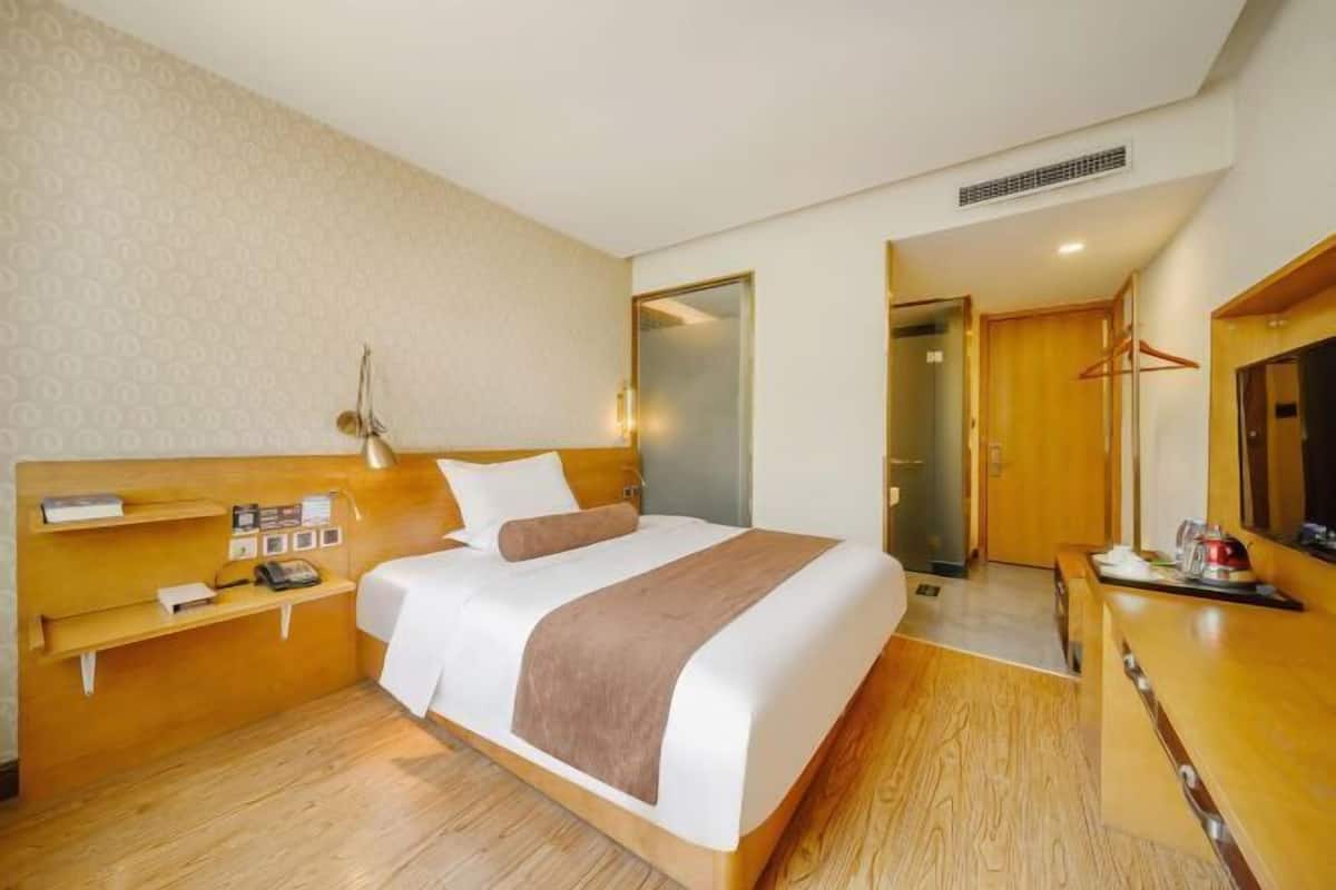 A hotel room with a bed, bedside tables, a desk, and a television.