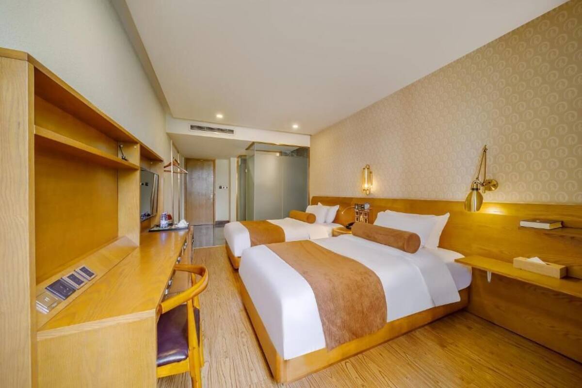 A hotel room with two beds, a desk, a chair, and a small table.