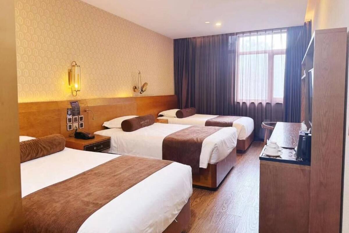 A hotel room with three beds, a wooden desk, a lamp, and a window with curtains.