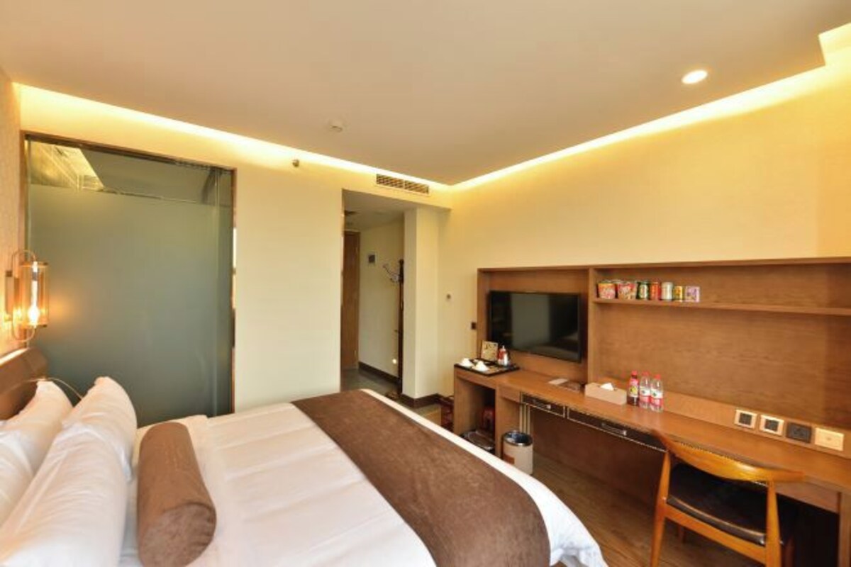 A hotel room with a bed, a desk with a television, a minibar, and a bathroom visible through an open door.