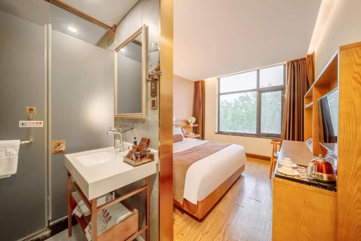 A hotel room with a shower, sink, bed, and a window with curtains.
