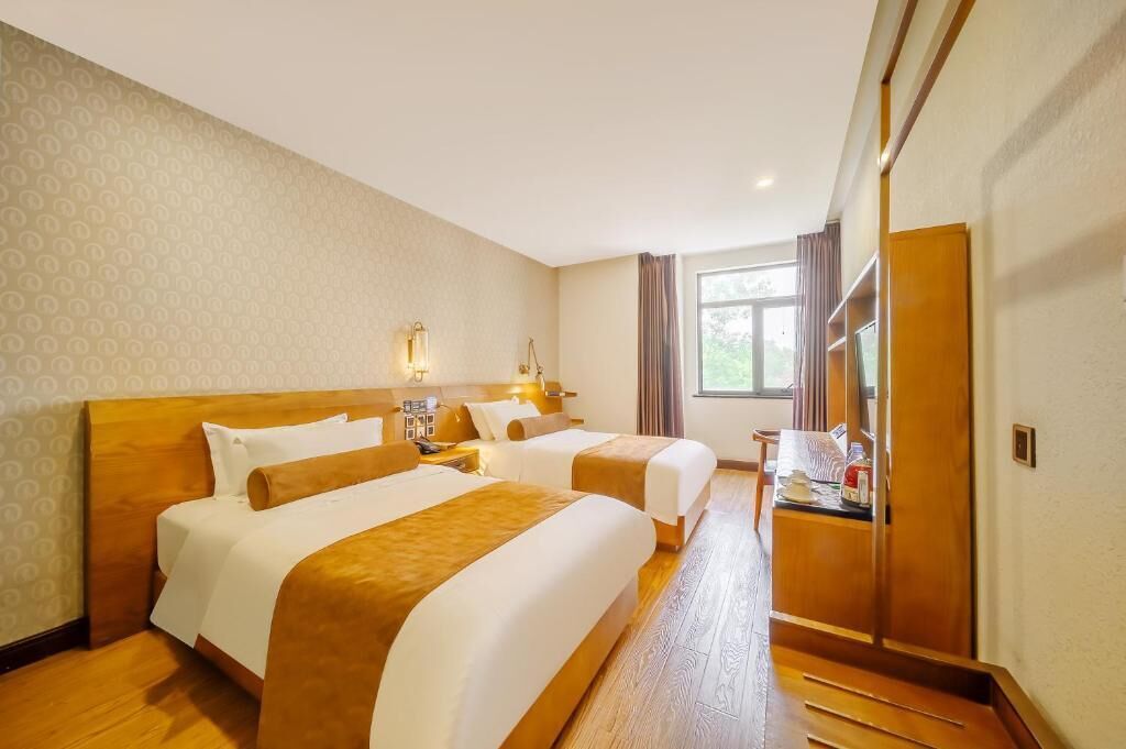 A hotel room with two beds, a desk, a mirror, and a window with curtains.