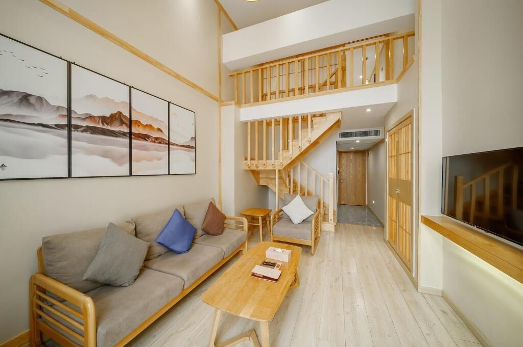 A modern living room with a sofa, coffee table, and a TV. A wooden staircase leads to an upper level.