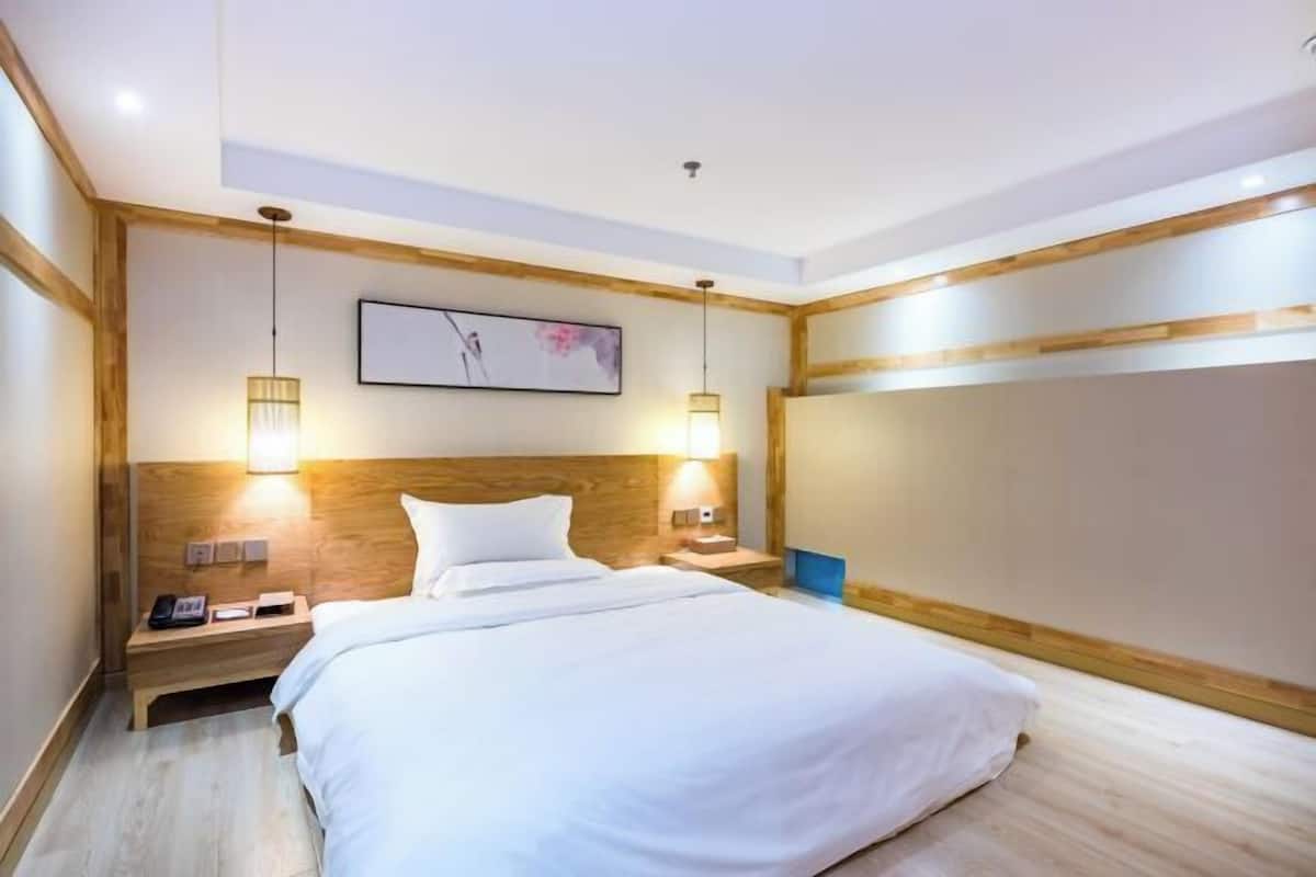 A modern hotel room with a wooden headboard, two bedside lamps, a large bed, and a framed picture on the wall.