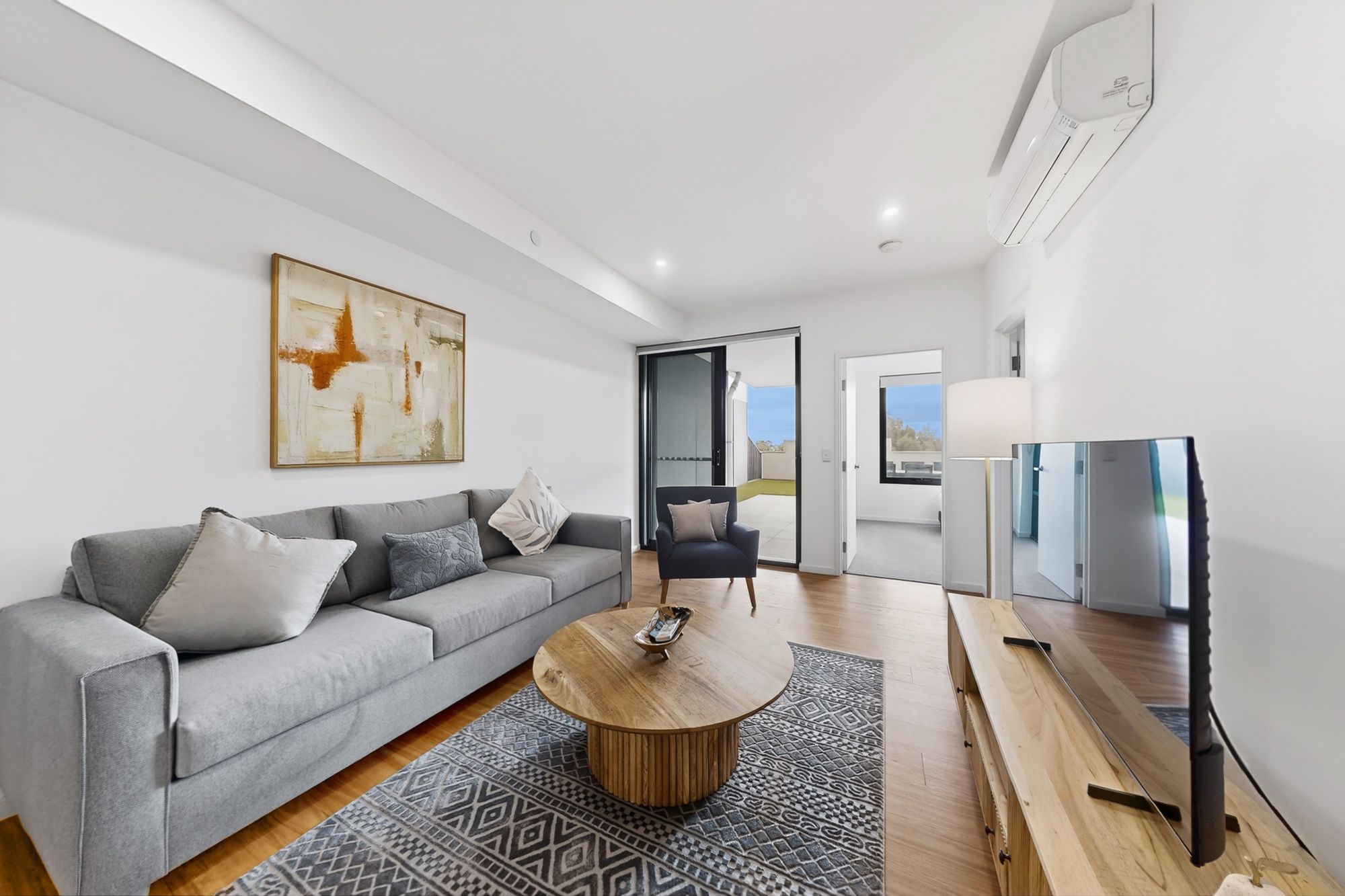 A modern living room with a grey sofa, a round wooden coffee table, and a television.