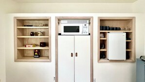 A compact kitchen with a microwave, a refrigerator, and built-in shelving with kitchenware.