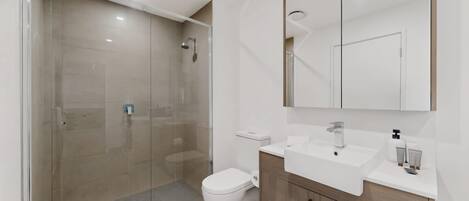 Une salle de bain moderne avec une douche à parois de verre, des toilettes, un lavabo avec un miroir au-dessus et des meubles en bois.