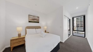 Ein Hotelzimmer mit einem Bett, zwei Nachttischen mit Lampen, einem Bild an der Wand und Blick durch eine Tür.