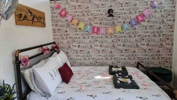A room with a brick wall, a bed with a floral bedspread, a 'Happy Birthday' banner, and a window with a view of trees.