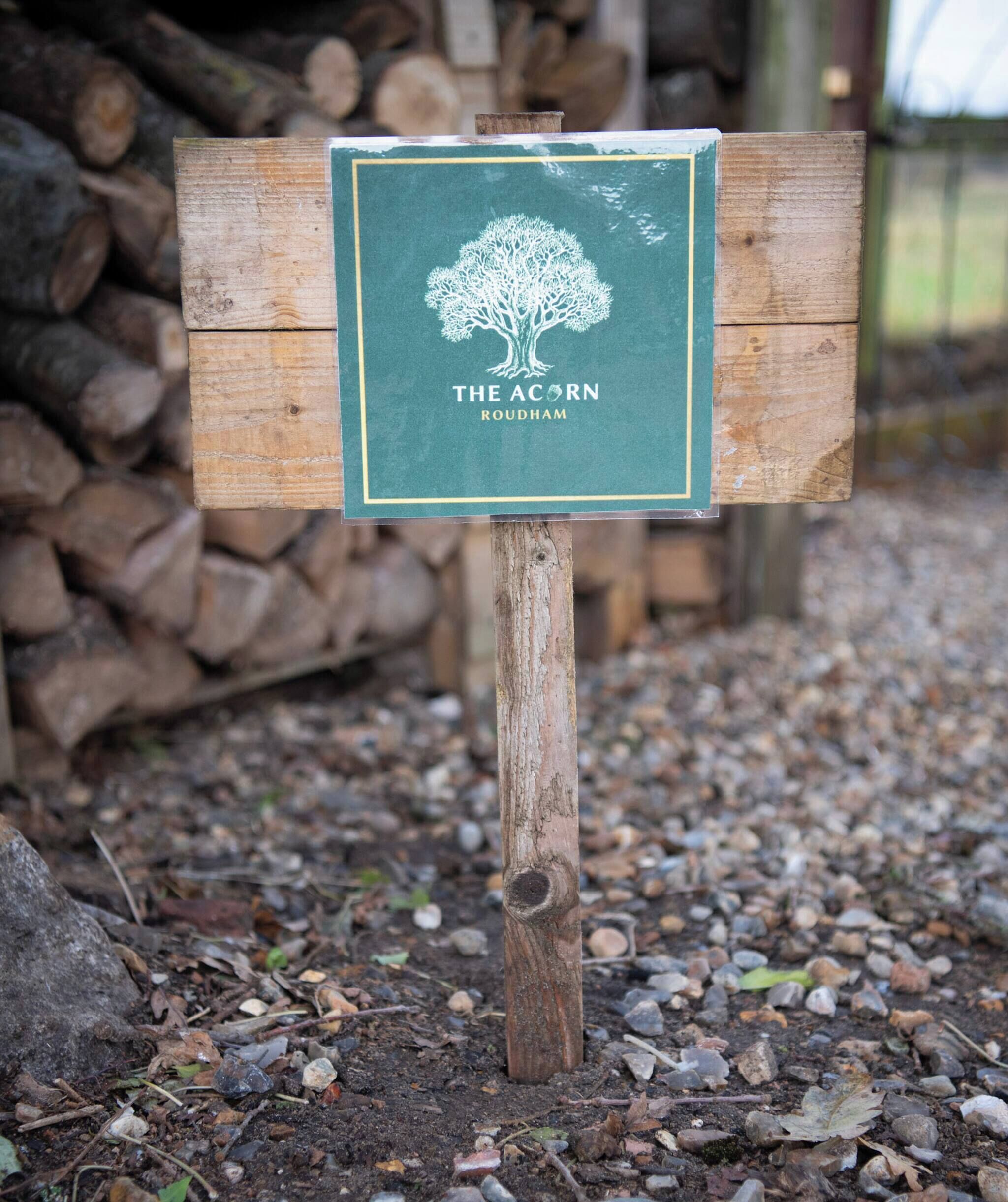 Een houten bord met een boomlogo en de tekst 'THE ACORN ROUDHAM' op een paal.