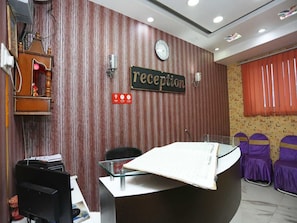 Un espace d’accueil avec un mur en bois, une horloge, un panneau d’identification, un bureau avec des papiers et des chaises violettes.