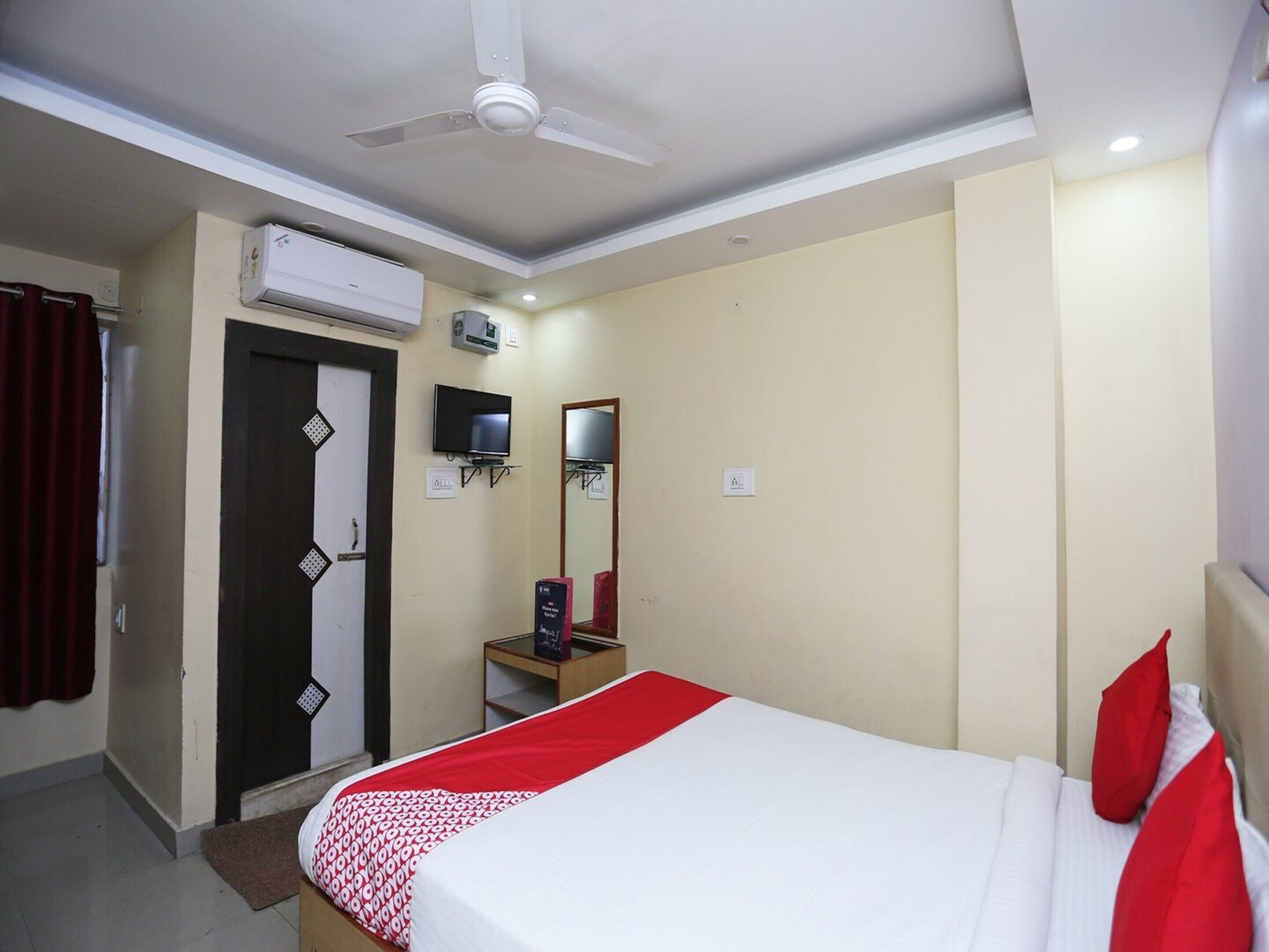 Ein Hotelzimmer mit einem Bett, einem Deckenventilator, einer Klimaanlage, einem Fernseher, einem Spiegel und einem kleinen Tisch.