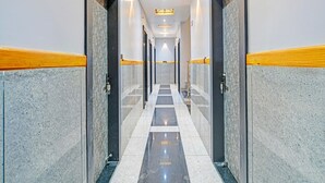 Um corredor comprido e estreito com paredes e portas de mármore, dando acesso a quartos.