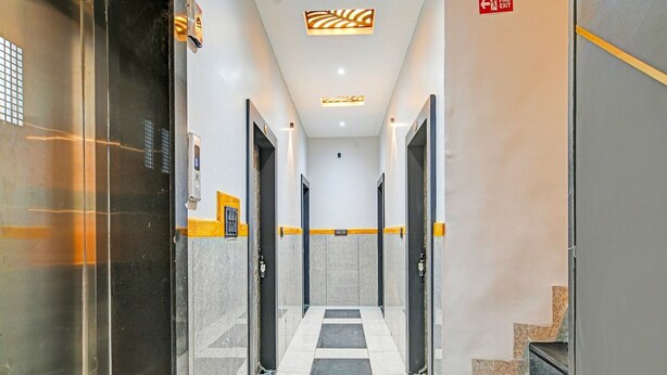 Um corredor com piso xadrez, portas de ambos os lados e sinalização de saída de incêndio.