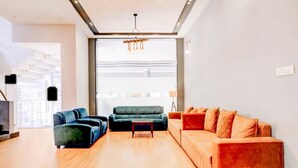 A modern living room with a wooden floor, a sofa set, a coffee table, and a large window with blinds. - Townhouse Oak Ulwe (Panvel)