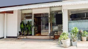 A building with a modern design, featuring a glass entrance, potted plants, and a seating area outside. - Townhouse Oak Ulwe (Panvel)