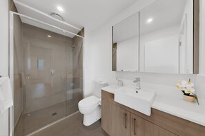 A modern bathroom with a glass-enclosed shower, a white toilet, and a vanity with a mirror and sink. - Stylish New Apt near Westfields with Parking (Cannington)