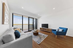 A modern living room with a sofa, a blue armchair, a TV, and a large sliding glass door leading to a balcony.