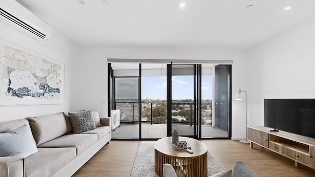 A modern living room with a sofa, a coffee table, a TV, and a balcony with a city view. - Newly Built Apartment Near Shops and Parks (Cannington)