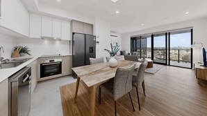 A modern kitchen with a dining area, large windows, and a view of the landscape. - Newly Built Apartment Near Shops and Parks (Cannington)