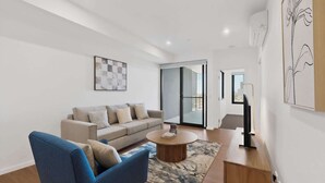 A modern living room with a sofa, armchair, coffee table, and artwork on the walls. - Bright Newly 2 Bed Apartment with Balcony Views (Cannington)
