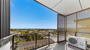 A balcony with a clear view of a residential area, a large window with a mesh screen, and an air conditioning unit. - Bright Newly 2 Bed Apartment with Balcony Views (Cannington)