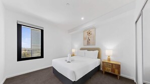 A bedroom with a bed, bedside lamps, a nightstand, a window, and a painting on the wall. - Bright Newly 2 Bed Apartment with Balcony Views (Cannington)