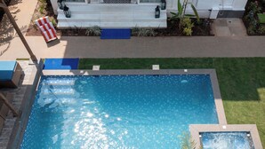 A rectangular swimming pool with a tiled edge, surrounded by a well-maintained lawn and a white building with steps leading up to a door. - ELIVAAS Fernweh 4 BHK with Pool (Assagao)
