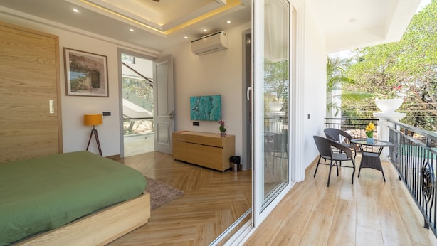 A modern bedroom with a bed, a dresser, a TV, and a balcony with chairs and a table. - ELIVAAS Fernweh 4 BHK with Pool (Assagao)