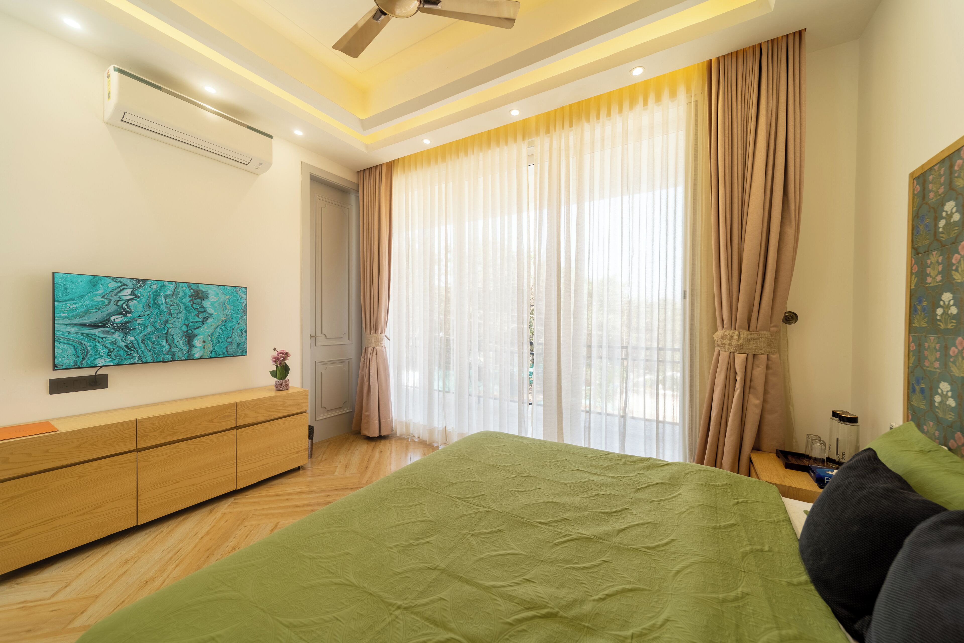 A bedroom with a bed, a TV, a ceiling fan, and a window with curtains.