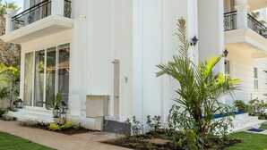 A white two-story house with a balcony, large windows, and a well-maintained lawn. - ELIVAAS Fernweh 4 BHK with Pool (Assagao)